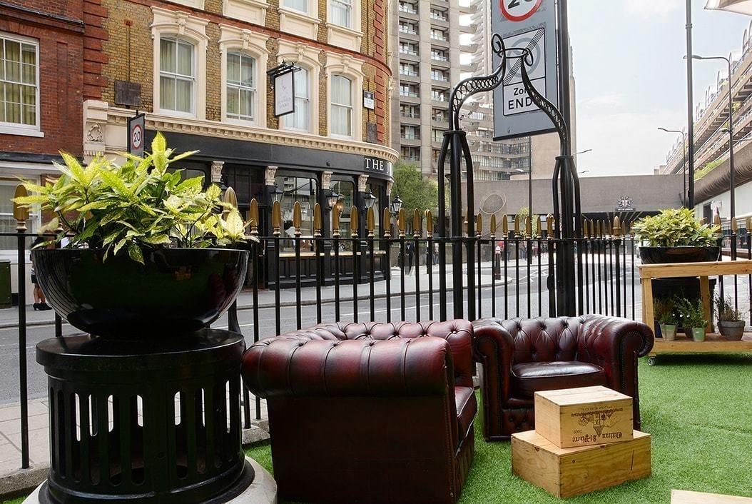 Montcalm Brewery Townhouse Hotel London Exterior photo The photo shows a street scene with a cozy outdoor seating area. There are two plush, dark leather couches arranged on green grass, creating a welcoming atmosphere. Surrounding the seating are large planters with vibrant plants. In the background, th