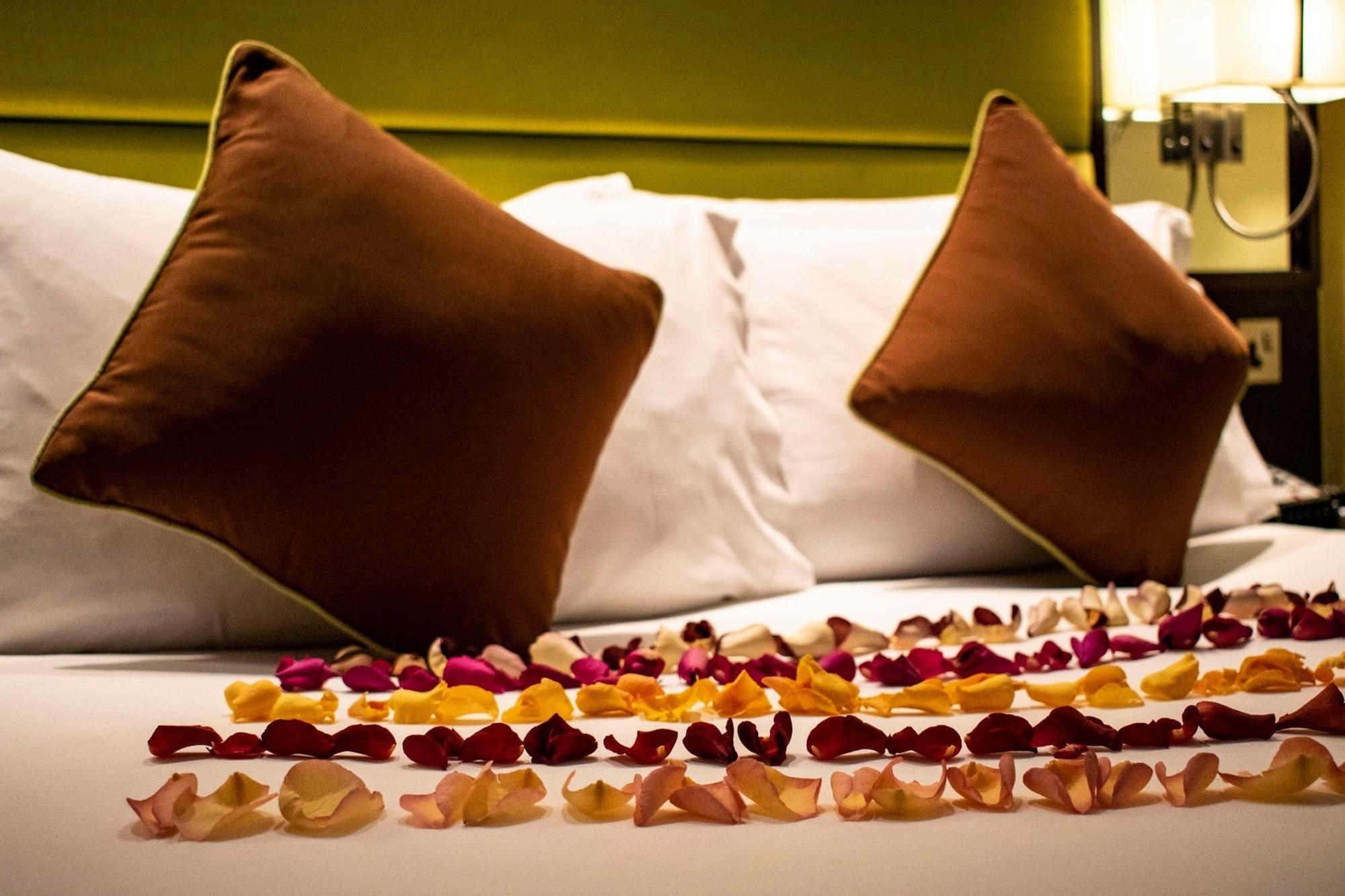 Montcalm Brewery Townhouse Hotel London Exterior photo The photo shows a neatly arranged bed with two white pillows and brown decorative cushions. Scattered across the bed is a decorative display of flower petals in various colors, including pink, yellow, and orange, creating a romantic or tranquil ambia