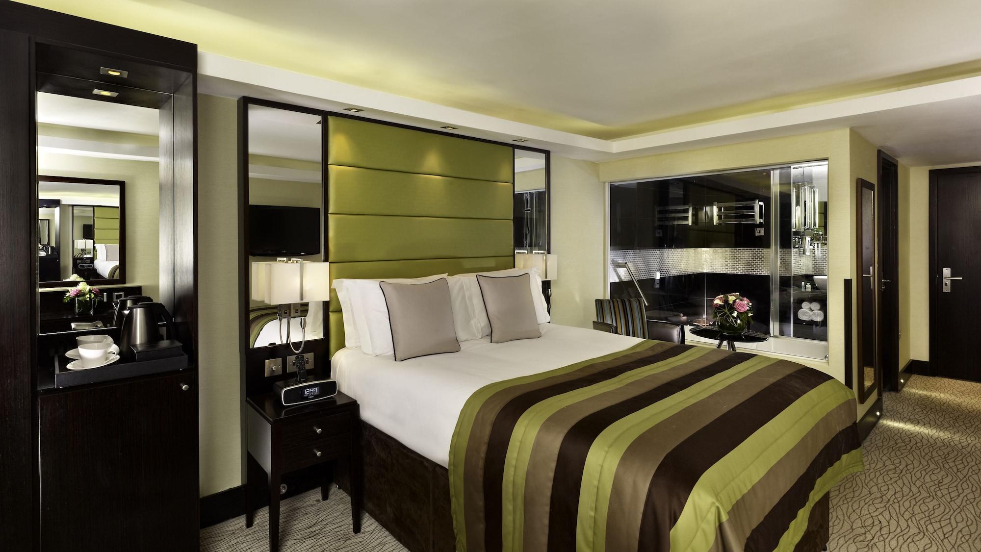 Montcalm Brewery Townhouse Hotel London Exterior photo The photo shows a modern hotel room designed with a sophisticated aesthetic. It features a comfortable double bed with a striped brown and green bedspread, complemented by two light gray decorative pillows. Behind the bed is an elegant headboard sect