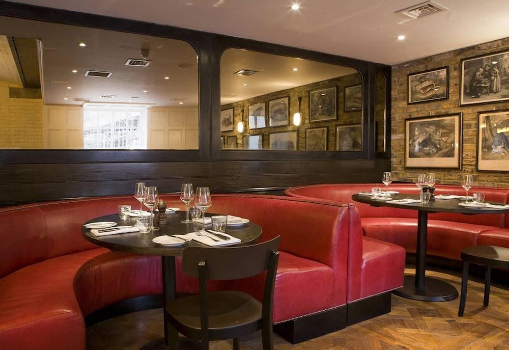 Montcalm Brewery Townhouse Hotel London Exterior photo The image shows the interior of a restaurant featuring a warm and inviting atmosphere. There are several round tables surrounded by black chairs, with red, upholstered booths lining the walls. The decor includes framed artwork hanging on the walls, a