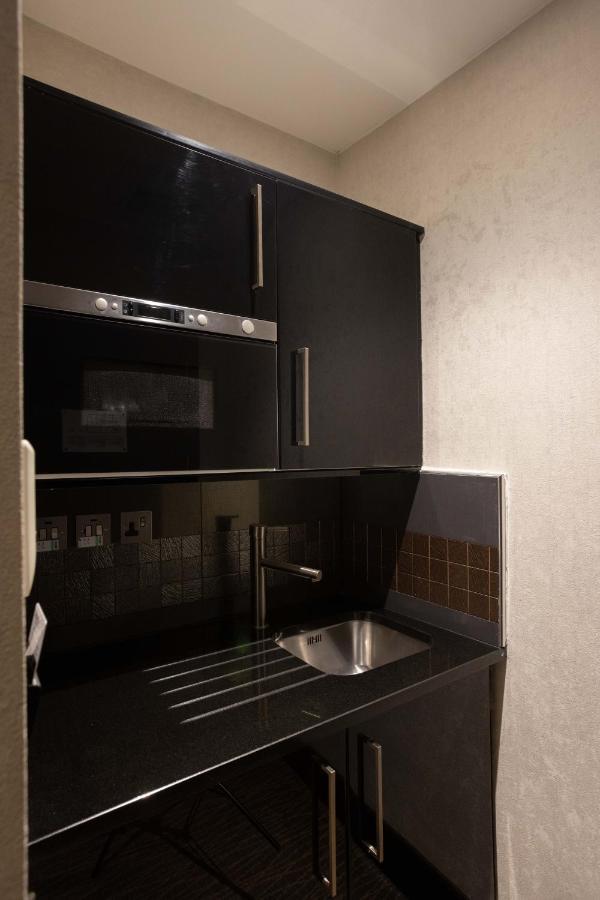 Montcalm Brewery Townhouse Hotel London Exterior photo The photo shows a modern kitchen setup with a dark color scheme. It features:

- A built-in microwave oven situated above a countertop.
- A sleek black cabinet beneath the microwave, which likely stores kitchen items.
- A stainless steel sink placed 