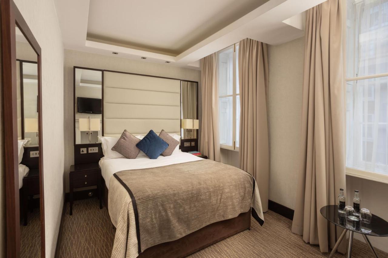 Montcalm Brewery Townhouse Hotel London Exterior photo The photo shows a cozy hotel bedroom. The room features a neatly made double bed with a beige bedspread and decorative pillows, including a blue one. There are bedside tables on either side of the bed with lamps. The walls are painted in a soft color