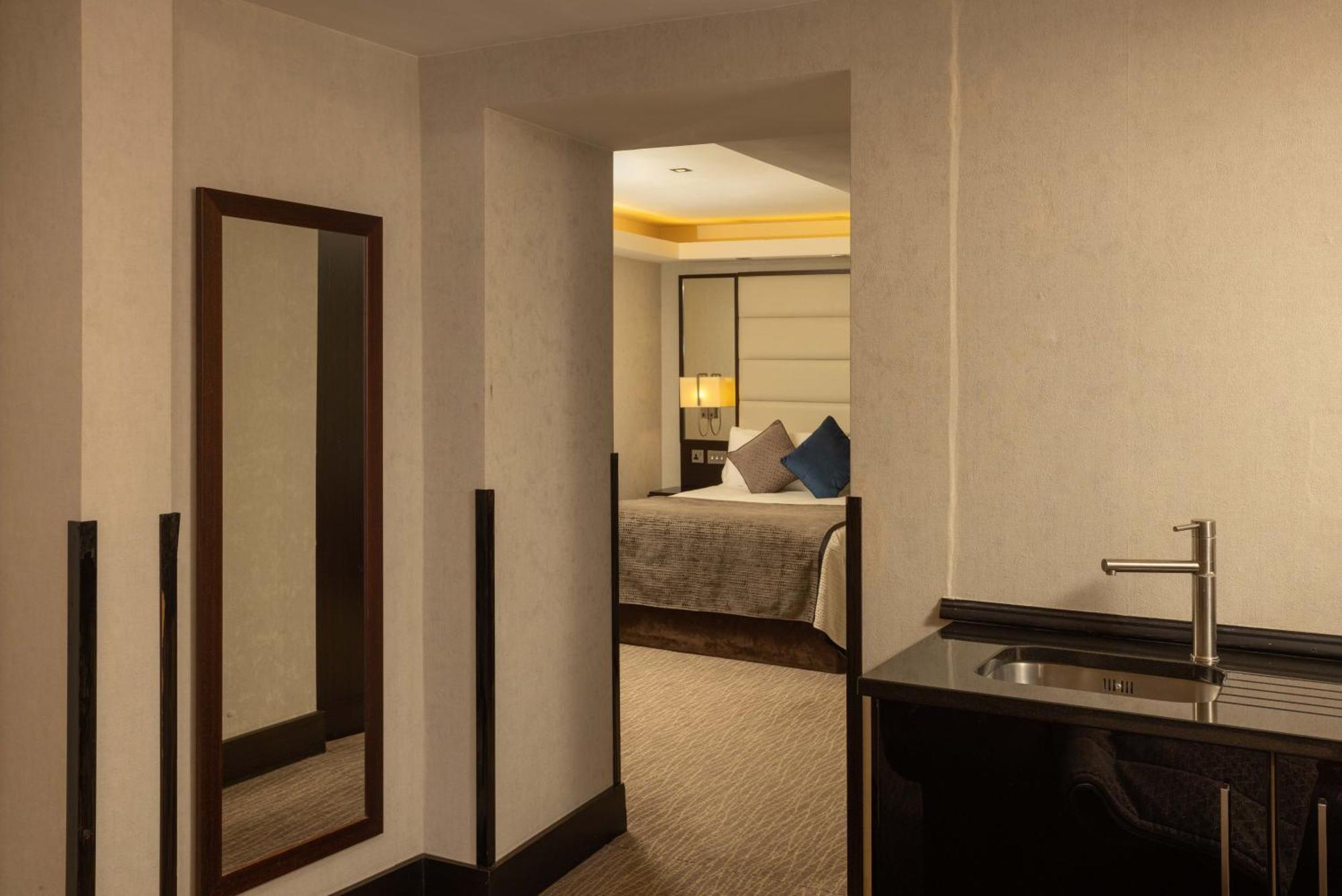 Montcalm Brewery Townhouse Hotel London Exterior photo The photo shows an interior space that appears to be part of a hotel room or suite. There is a doorway leading into a bedroom area, where a bed with decorative pillows is visible. In the foreground, there's a tall mirror on the left side and a small 