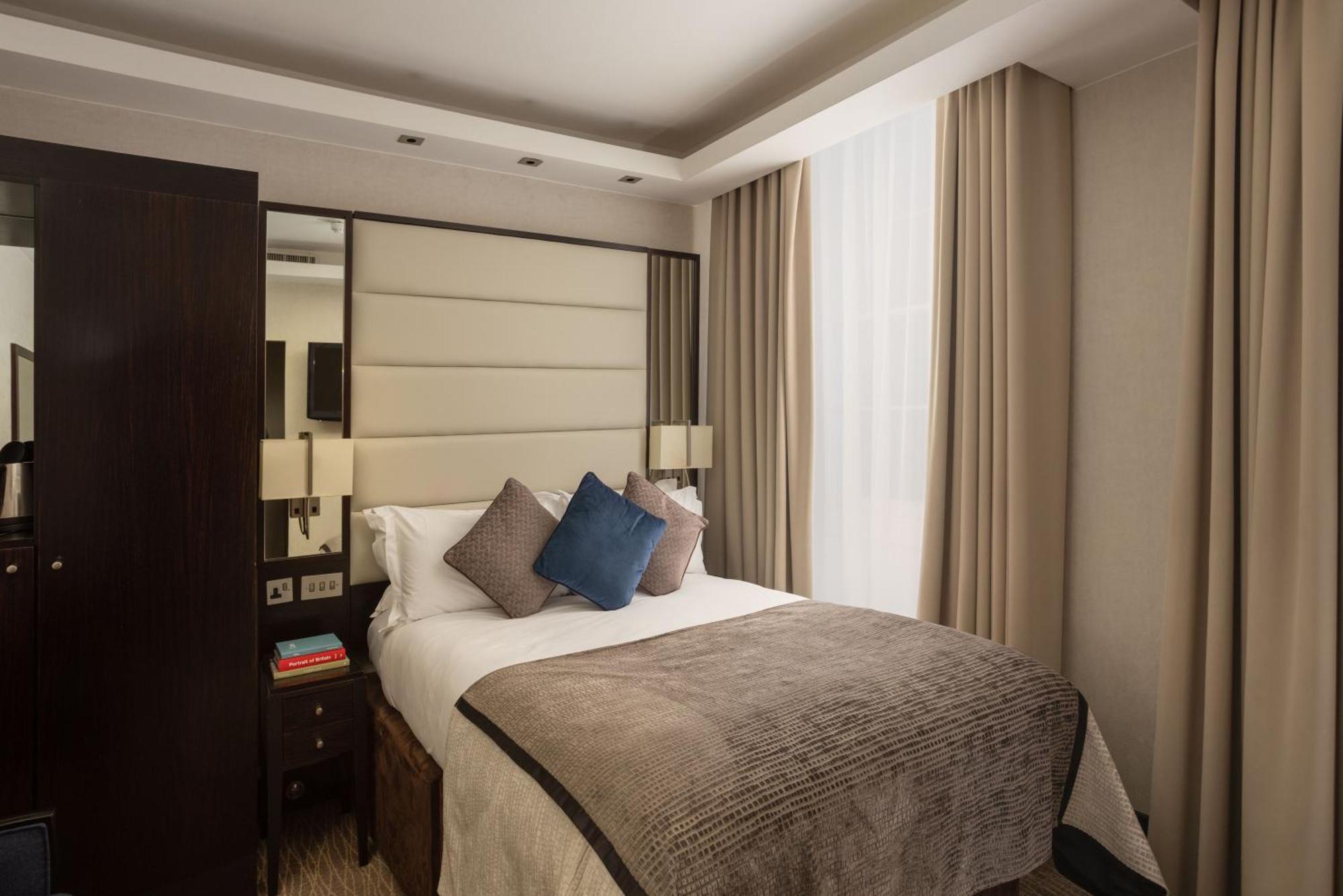 Montcalm Brewery Townhouse Hotel London Exterior photo The photo shows a modern hotel room with a cozy design. It features a double bed with a light-colored headboard and a soft, stylish blanket. There are decorative pillows on the bed, including a blue one. On either side of the bed, there are small nig