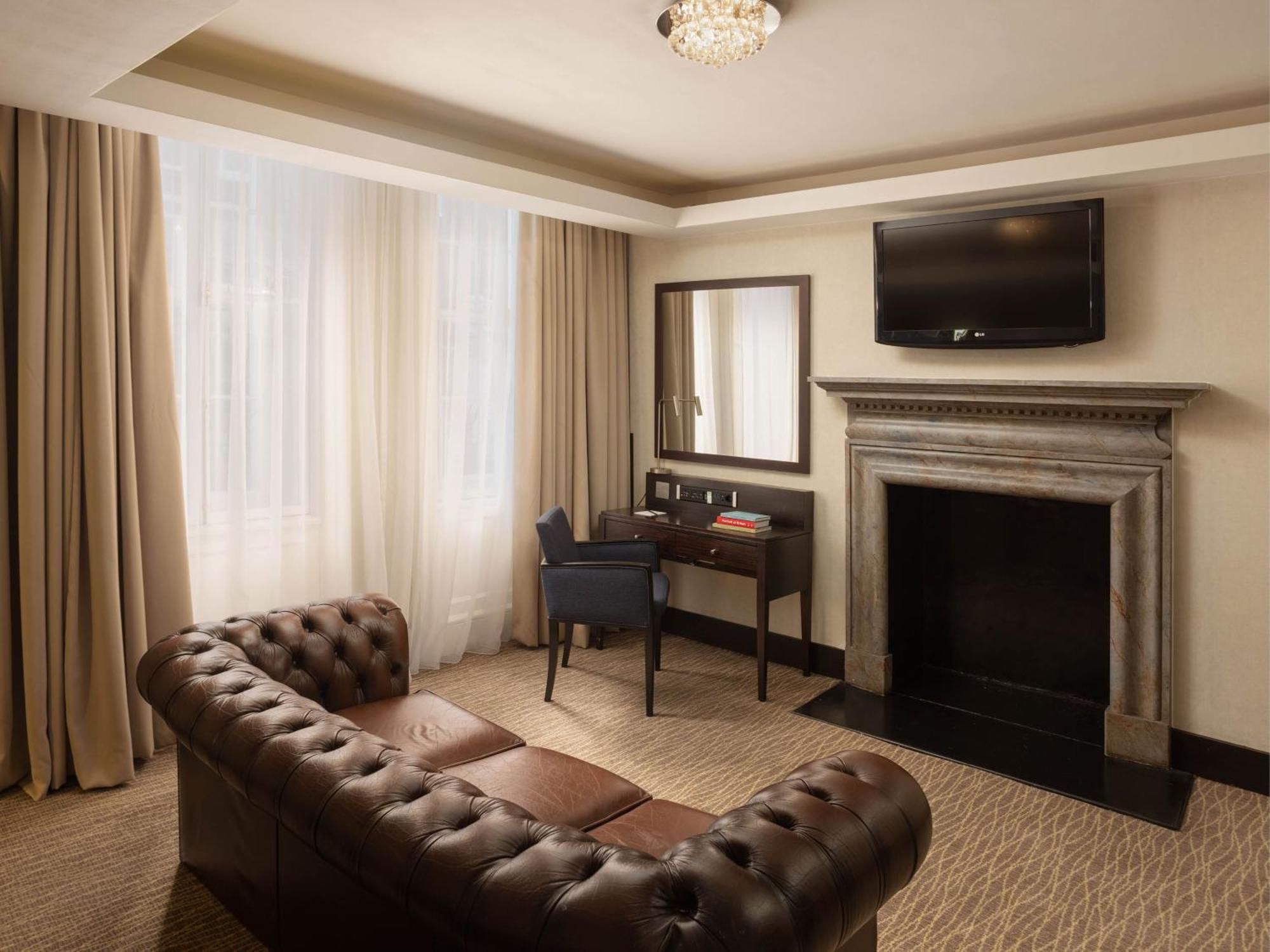 Montcalm Brewery Townhouse Hotel London Exterior photo The photo shows a cozy and elegantly designed room. There is a comfortable brown leather sofa with tufted detailing. A small desk and chair are positioned near a mirror, providing a space for work or personal grooming. On the wall, a flat-screen TV i