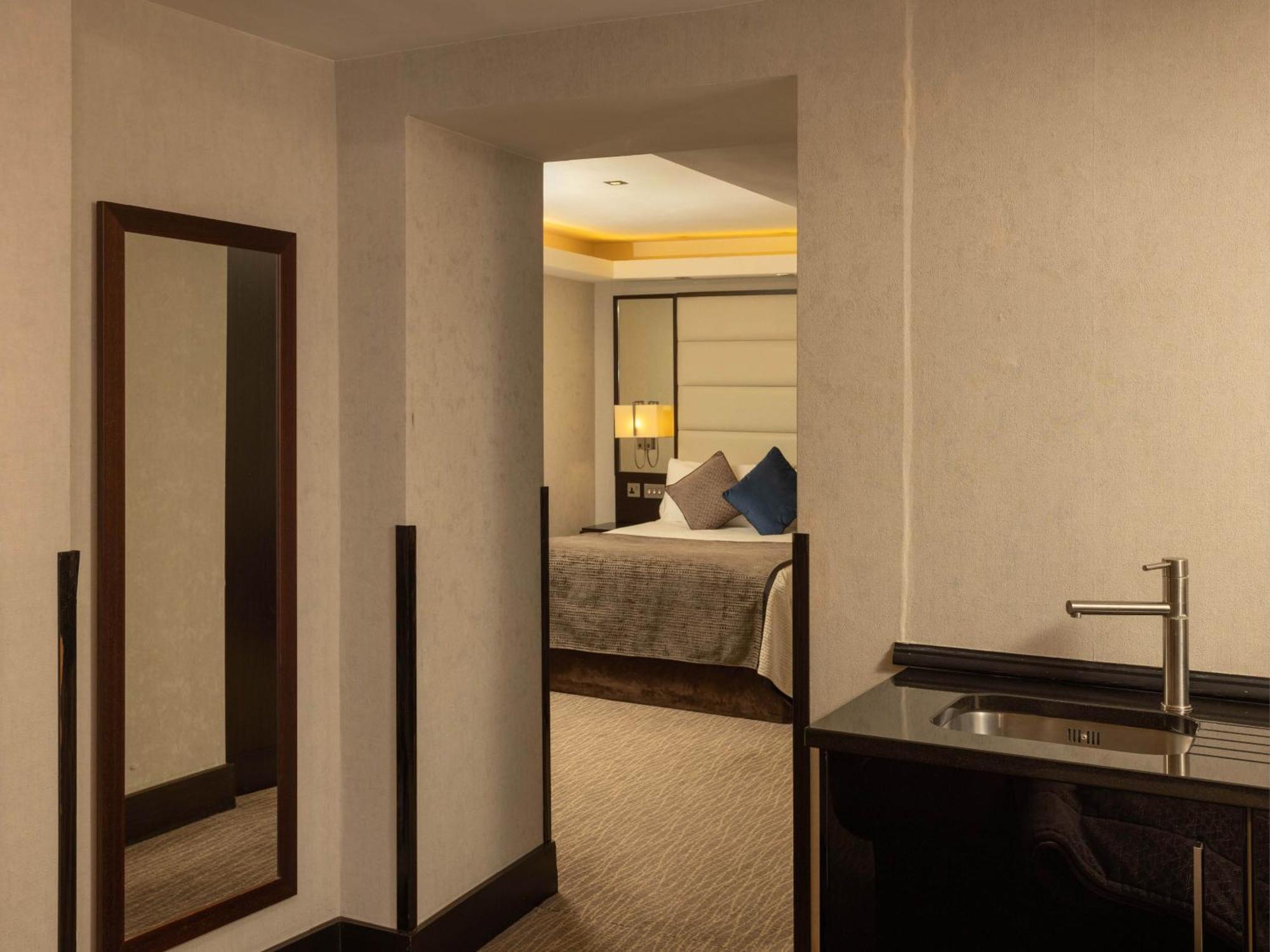 Montcalm Brewery Townhouse Hotel London Exterior photo The photo shows an interior space that appears to be a hotel room or a suite. There is a doorway leading to a bedroom visible in the background, where a bed with decorative pillows can be seen. To the side, there is a small wet bar or kitchenette are