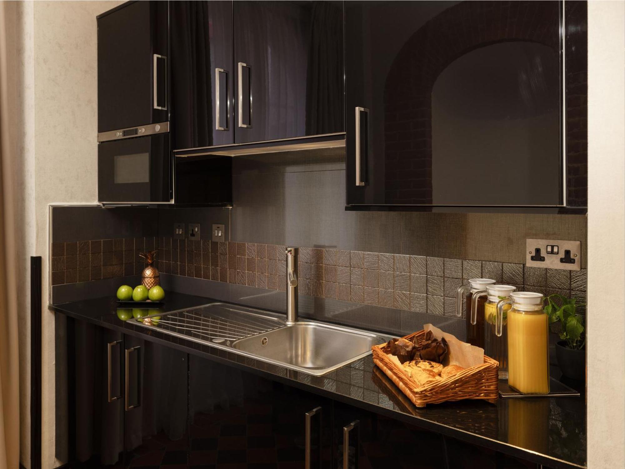 Montcalm Brewery Townhouse Hotel London Exterior photo The photo shows a modern kitchen with sleek black cabinetry and a glossy finish. The kitchen features a stainless steel sink with a contemporary faucet, set against a dark, textured countertop. Above the counter, there are cabinets that match the cou