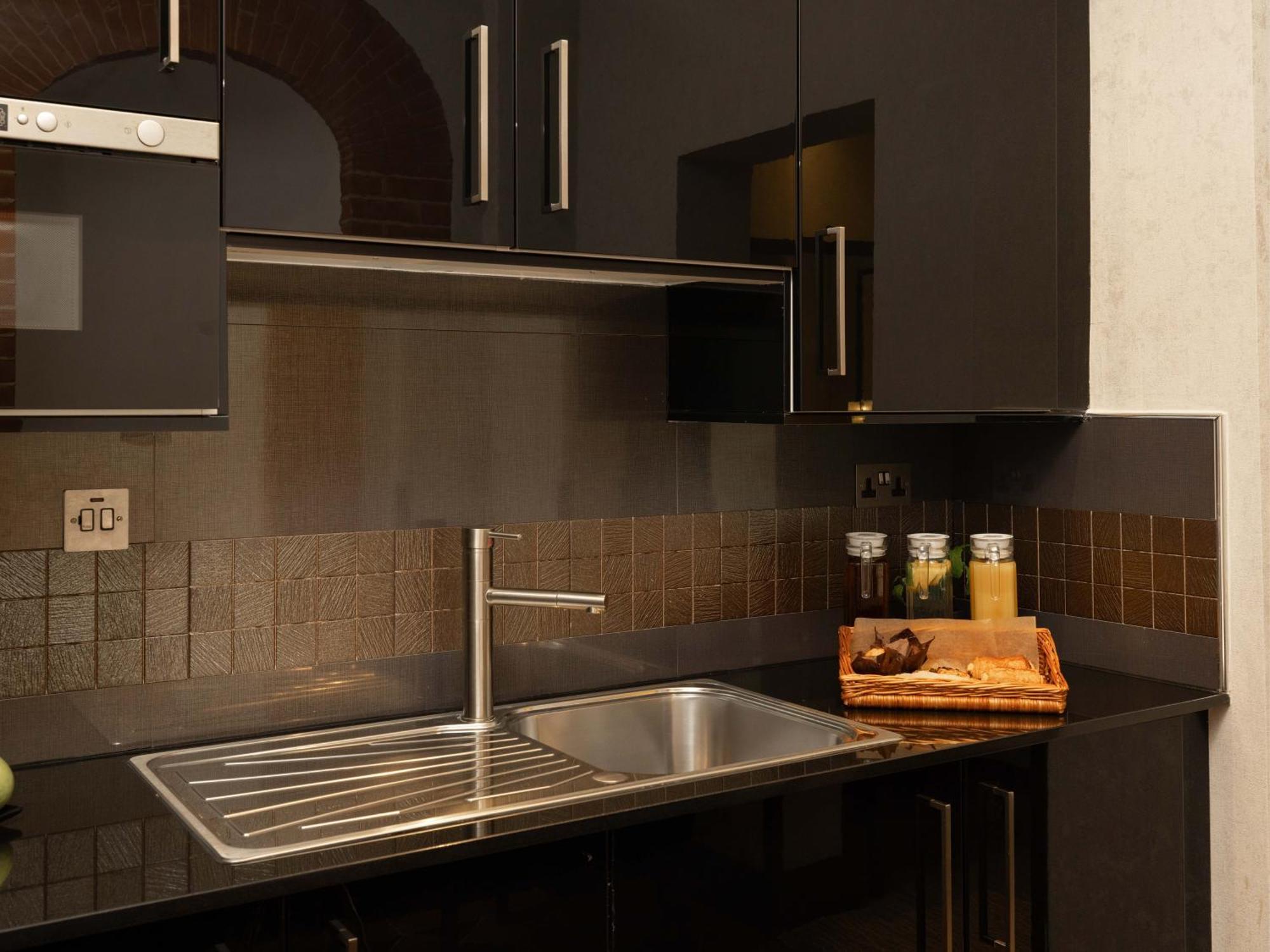 Montcalm Brewery Townhouse Hotel London Exterior photo The photo shows a modern kitchen with a sleek design. It features dark cabinetry with a glossy finish and stainless steel handles. There is a stainless steel sink with a simple faucet, and a countertop made of black material. Above the sink, there ar