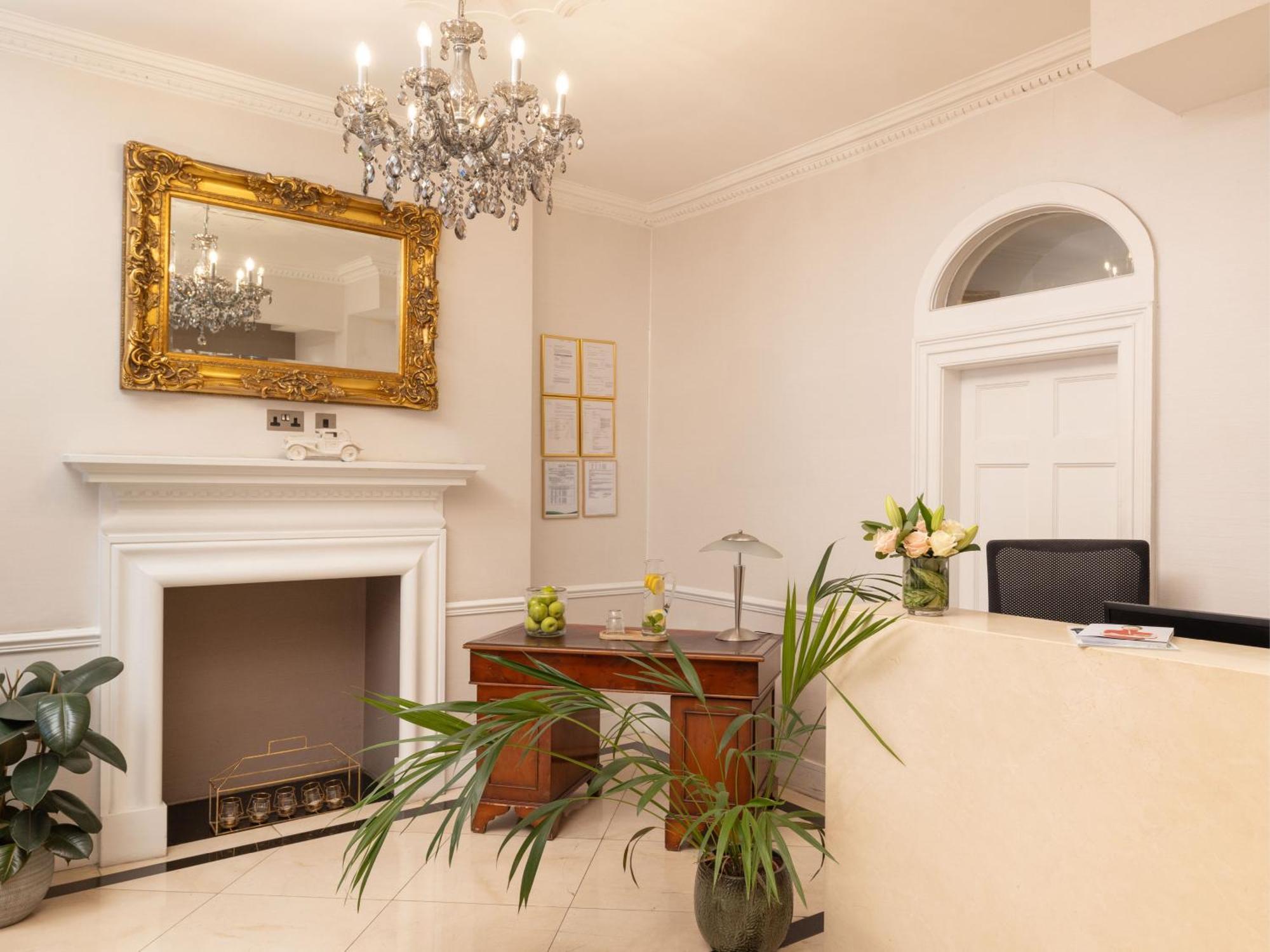 Montcalm Brewery Townhouse Hotel London Exterior photo The photo shows a stylish reception area. There is a decorative chandelier hanging from the ceiling, providing elegant lighting. A large, ornate mirror is mounted on the wall beside the fireplace, which features a simple, classic design. In front of 