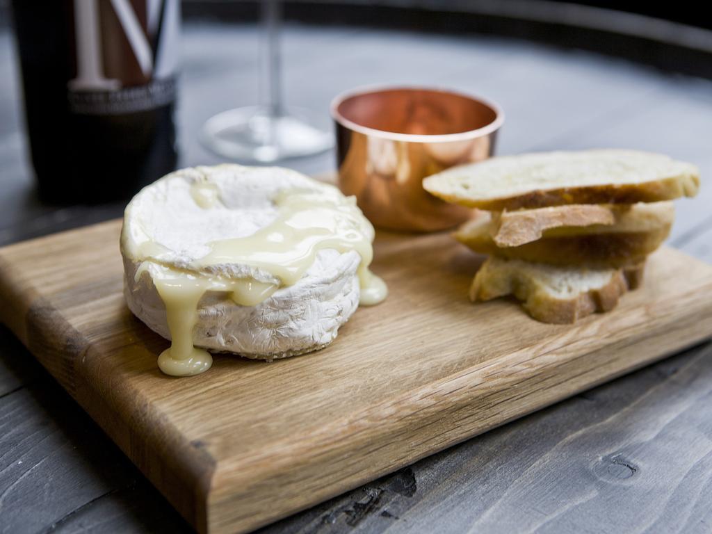 Montcalm Brewery Townhouse Hotel London Exterior photo The photo features a wooden serving board with several items. There is a round cheese, likely Brie or a similar soft cheese, that appears to be melting and dripping slightly. Next to the cheese, there is a small copper cup that might contain a sauce 