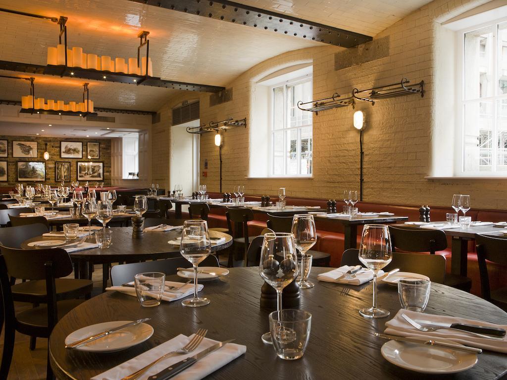 Montcalm Brewery Townhouse Hotel London Exterior photo The photo shows a restaurant interior featuring a warm and inviting atmosphere. It has several round wooden tables set for dining, each with neatly arranged plates, utensils, and glasses. The lighting is soft, with overhead fixtures providing a cozy 