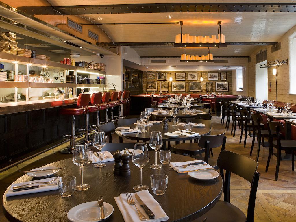 Montcalm Brewery Townhouse Hotel London Exterior photo The photo shows the interior of a stylish restaurant. It features several round tables set with white plates, glasses, and silverware, all neatly arranged for dining. The decor includes a modern design with wooden floors and a mix of lighting fixture