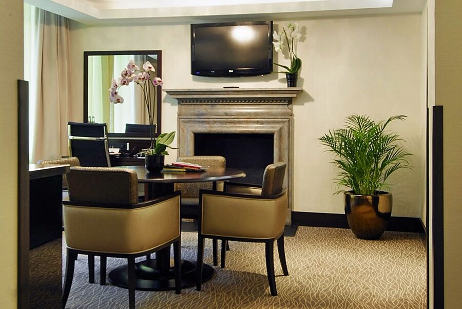 Montcalm Brewery Townhouse Hotel London Exterior photo The photo shows a modern and stylish room with a dining or meeting area. There is a round table surrounded by four upholstered chairs. A flat-screen television is mounted on the wall above a decorative fireplace. To the side, there is a mirror reflec