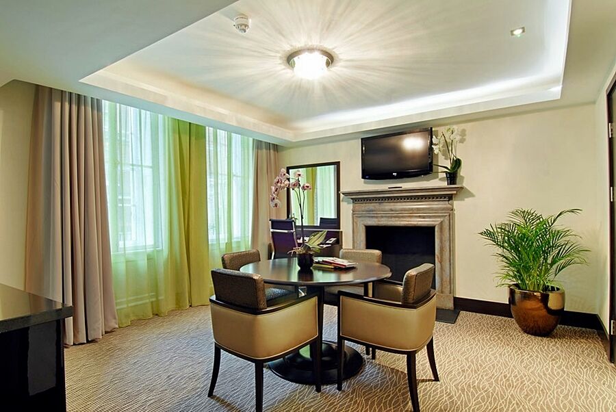 Montcalm Brewery Townhouse Hotel London Exterior photo The photo shows a well-furnished room, likely a hotel suite or a modern living space. It features a round dining table with four comfortable chairs. The walls are adorned with light-colored decor, and there are large windows with sheer and solid curt