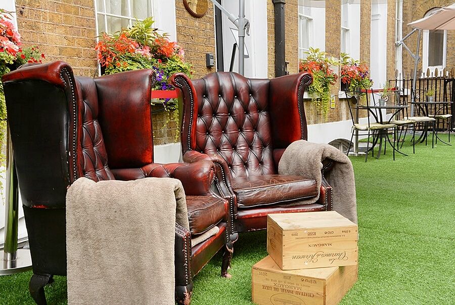 Montcalm Brewery Townhouse Hotel London Exterior photo The photo depicts two large, elegant armchairs with a classic design, featuring rich burgundy leather upholstery and button tufting. They are positioned in a cozy outdoor setting, with lush green artificial grass beneath them. Next to the chairs, the